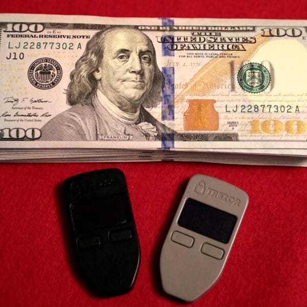 Two Trezor One hardware wallets beside U.S. cash
