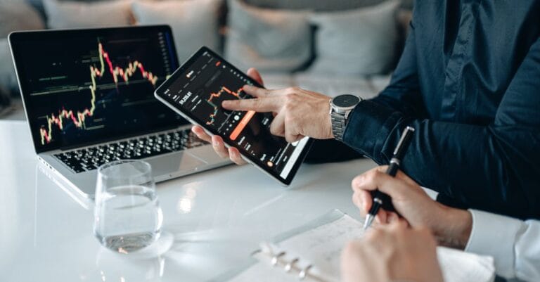 Professionals reviewing financial market data on a tablet and laptop