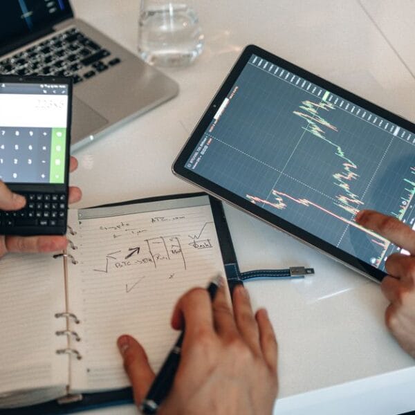 Two professionals analyzing financial charts on a digital tablet and laptop