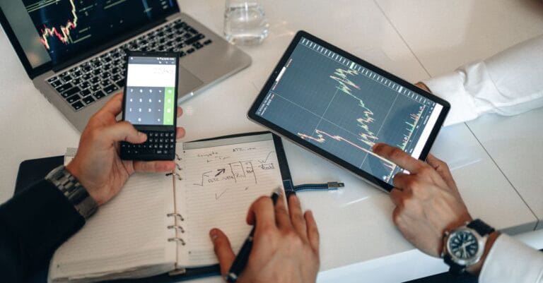 Two professionals analyzing financial charts on a digital tablet and laptop