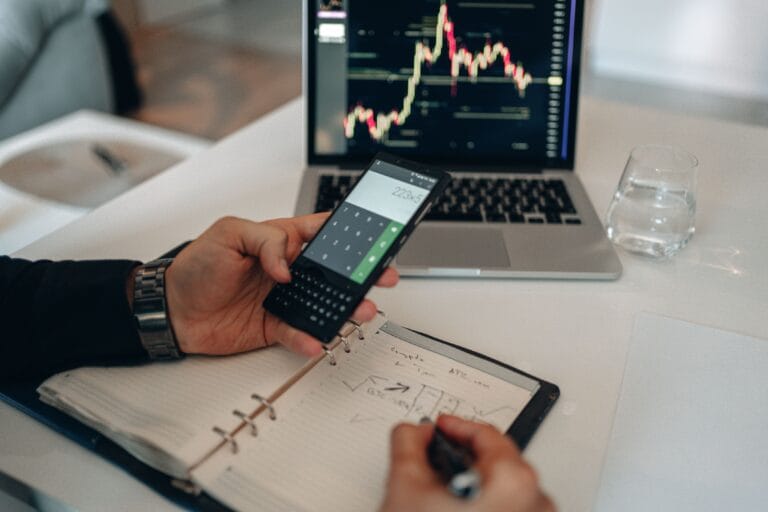 Person using a calculator and laptop with financial charts while investigating an incorrect portfolio balance