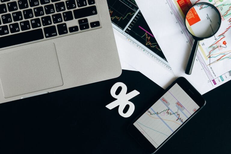 Financial analysis workspace with laptop, smartphone and printed charts for comparing crypto portfolio trackers