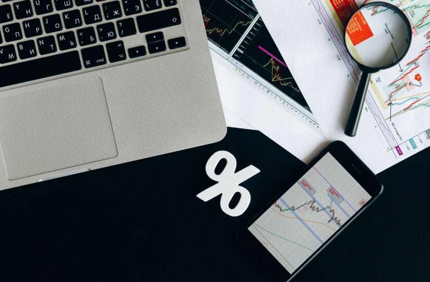 Financial analysis workspace with laptop, smartphone and printed charts for comparing crypto portfolio trackers