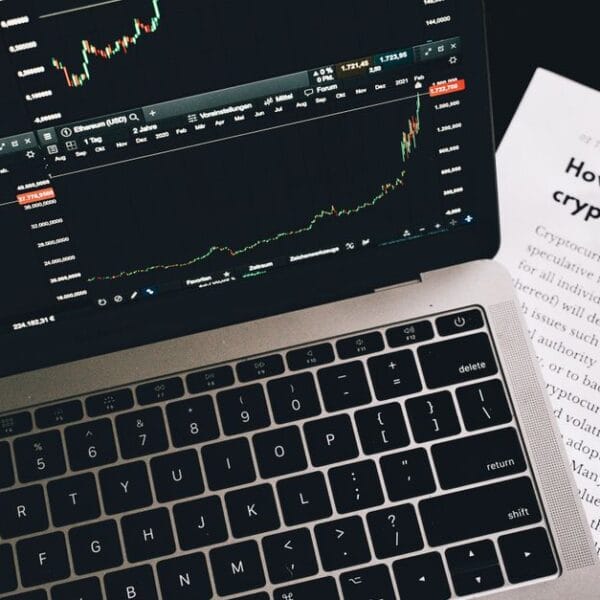 Investment research paper beside a laptop displaying financial market charts