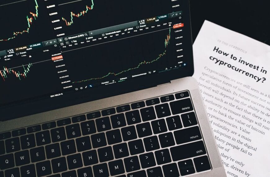 Investment research paper beside a laptop displaying financial market charts