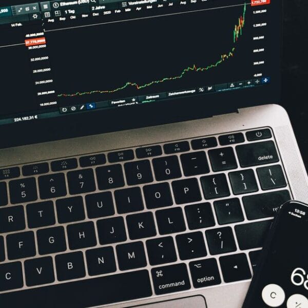 Laptop and smartphone showing cryptocurrency market data beside physical crypto tokens