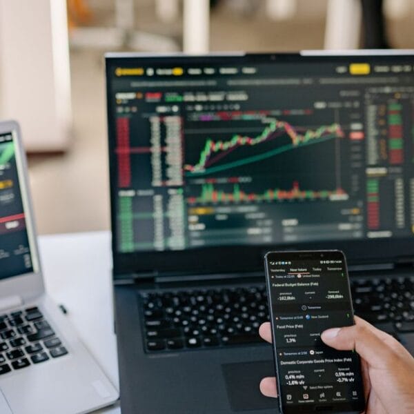 Professional using two laptops and a smartphone to review financial market information