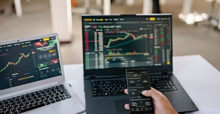 Professional using two laptops and a smartphone to review financial market information