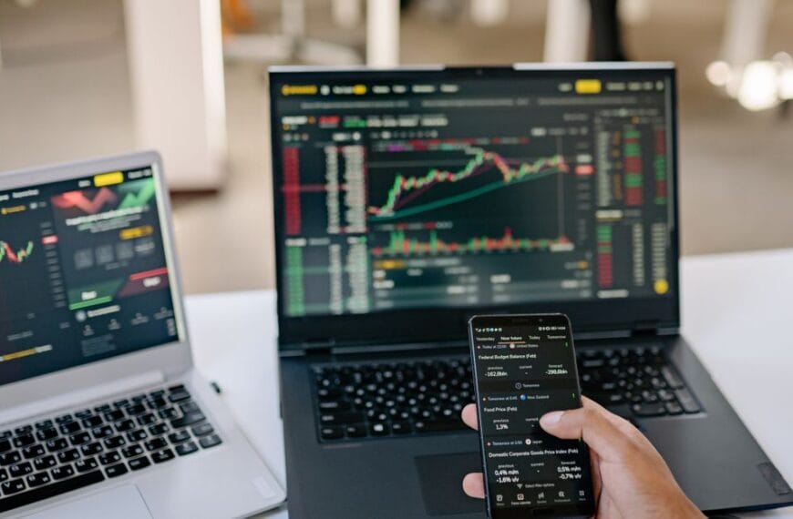 Professional using two laptops and a smartphone to review financial market information