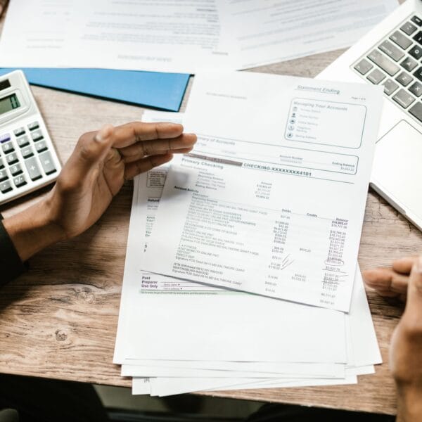 Hands reviewing financial documents beside a calculator and laptop during a crypto transaction audit